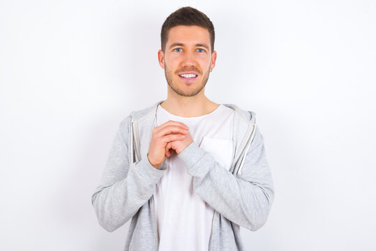 Dreamy charming young caucasian man wearing casual clothes over white background with pleasant expression, keeps hands crossed near face, excited about something pleasant.