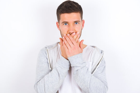Upset young caucasian man wearing casual clothes over white background, covering her mouth with both palms to prevent screaming sound, after seeing or hearing something bad.