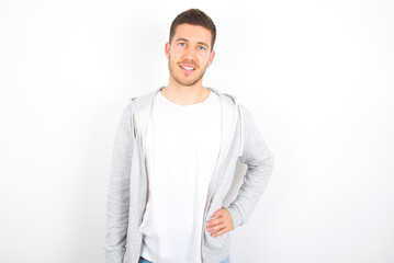 Studio shot of cheerful young caucasian man wearing casual clothes over white background  keeps hand on hip, smiles broadly.