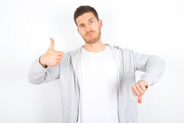 young caucasian man wearing casual clothes over white background  feeling unsure making good bad sign. Displeased and unimpressed.