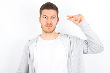 Upset young caucasian man wearing casual clothes over white background  shapes little gesture with...