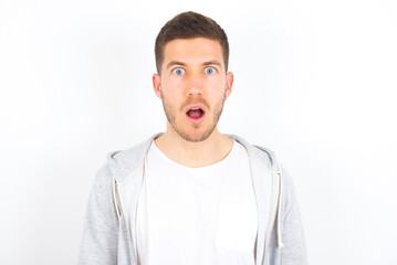 Fototapeta premium Emotional attractive young caucasian man wearing casual clothes over white wall with opened mouth expresses great surprise and fright, stares at camera. Unexpected shocking news and human reaction.