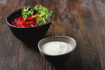 Traditional beetroot soup in a brown plate with Temyan, sour cream. Dark wood background. free space text.