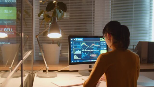 Businesswoman examining stock market analysis on computer screen while working late at night in office