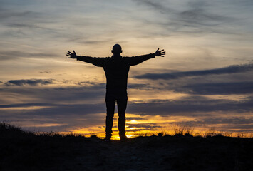 Silhouette of man standing with stretched out hands against the romantic sunset sky, concept of joy...