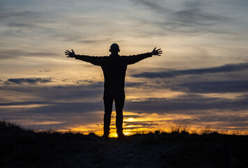 Silhouette of man standing with stretched out hands against the romantic sunset sky, concept of joy and happiness