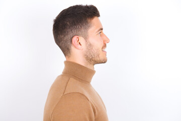 Profile portrait of nice young caucasian man wearing knitted turtleneck over white background look empty space toothy smile