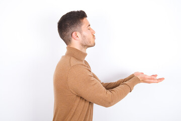 Profile side view view portrait of attractive young caucasian man wearing knitted turtleneck over white background sending air kiss