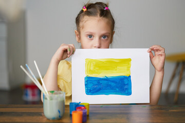 Sad child girl draws a picture of the war in Ukraine. Bright drawing with colors of the State flag of Ukraine, yellow and blue. Stop the war, save the world