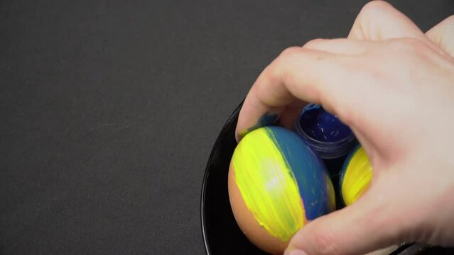 Girl paints Easter eggs in yellow-blue color. Chicken eggs are painted by a female hand in the color of Ukraine. Tassel, art, sacred eggs, national flag. Lots of fresh raw chicken eggs. Omelette.