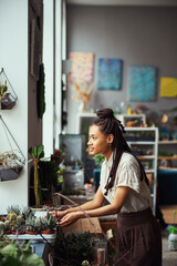 Attractive florist leaning towards potted plants in the nursery tray