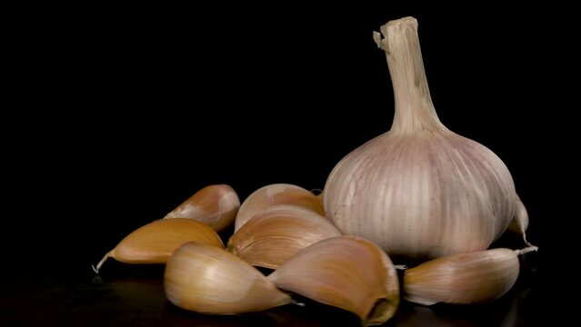 head of garlic surrounded by garlic cloves rotates on a black background 