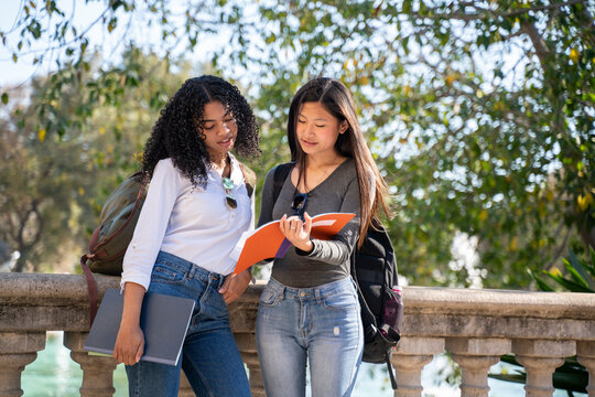 Two young female students in the street looking at their notebooks