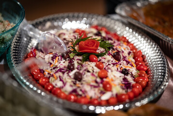 Shredded carrots, green and red cabbage salad decorated with olives and cherry tomatoes served in silver colored plate for catering of an event