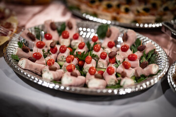 Tapas platter made out of small cream cheese ham wrapped bites served in silver color plate garnished with cherry tomatoes presented on the catering of an event
