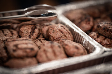 Traditional Bulgarian barbecued ground meat balls called kyufte served in a catering setting placed in aluminum foil pan