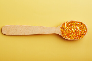 Vitamin D3 in a wooden spoon on a bright yellow background