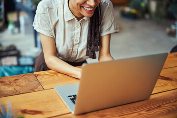 Merry young lady with cornrows working on her laptop