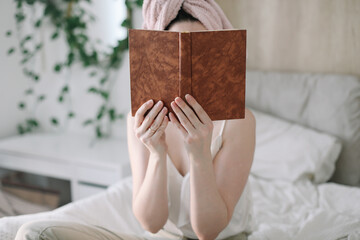 Morning book reading. Young woman with a towel on head reading book in bed in the morning 