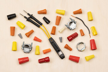 Horizontal flat layout of assorted color wire nuts, connectors, electricity tester, and wire on light wood textured background