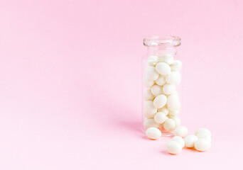White homeopathic capsules in a glass bottle on a pink background. Alternative medicine. Copyspace for text
