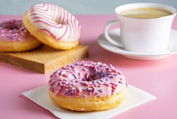 Three delicious fresh glazed donuts and cup of fresh hot coffee on pink background. Selective focus.