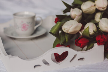 Sill life spring white and red tulips on a white sheet with wooden tray and cup of coffee in a hand painted cup and saucer