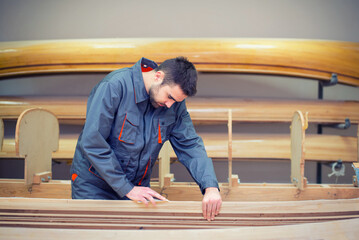 Young carpenter making wooden canoe in his workshop.