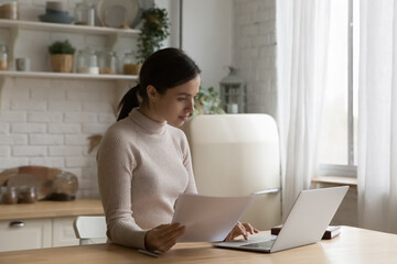 Woman working from home seated at table in domestic kitchen use laptop, prepare official papers...