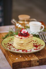 delicious pancakes with syrup in a stack and flower decoration on top a wooden table.