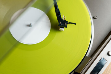 Closeup view of a tonearm and turntable playing color yellow vinyl record.