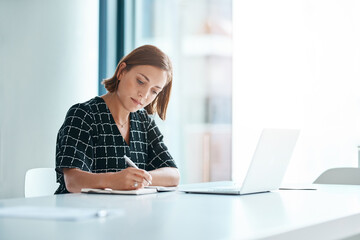 Dedication level A plus. Cropped shot of a focused young businesswoman writing on a notebook in an...