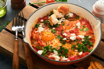 Shakshuka Homemade fried eggs poached in sauce of tomatoes, olive oil, peppers, onion and garlic in iron frying pan on old grey slate background. Traditional cuisine of Israel. Late breakfast concept