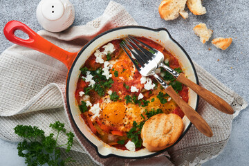 Shakshuka Homemade fried eggs poached in sauce of tomatoes, olive oil, peppers, onion and garlic in iron frying pan on old grey slate background. Traditional cuisine of Israel. Late breakfast concept