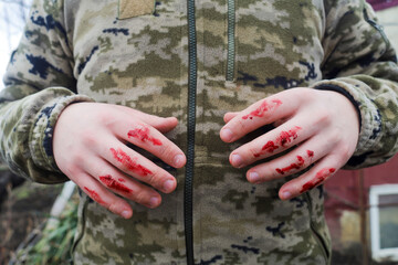 Concept. A soldier of the Ukrainian Army in camouflage, defending his homeland and citizens, stands with bloody hands.