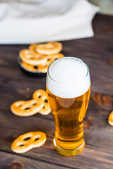 Glass of beer with foam and salty pretzels on a wooden table. Vertical view. Close-up