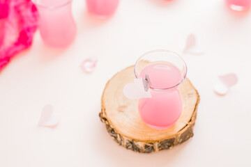 Pink cocktail in a glass on a tree trunk and paper hearts on a pink background. Drinks for lovers