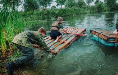 Dzieci pływają na samodzielnie zbudowanych tratwach na obozie sportowym, survivalowym. Współpraca w grupie w przeprawie tratwą na drugą stronę rzeki