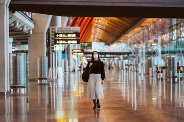 Tourist woman at the airport waiting for her flight. Wearing a mask for covid 19 protection doing a videocall with her tablet. Lifestyle. Travel