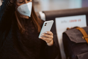 Tourist woman at the airport waiting for her flight. Wearing a mask for covid 19 protection using her smartphone while waiting. Lifestyle. Travel