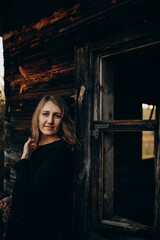 beautiful Ukrainian girl in black clothes near the old wooden house. The war in Ukraine. Portrait of a woman on a dark wooden background. Old abandoned wooden house. Old wooden window frame