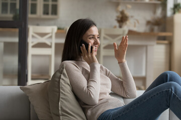 Happy beautiful young woman relax on sofa holds smartphone taking to friend, share news enjoy pleasant personal conversation. Mobile network operator usage, phone call activity, communication concept