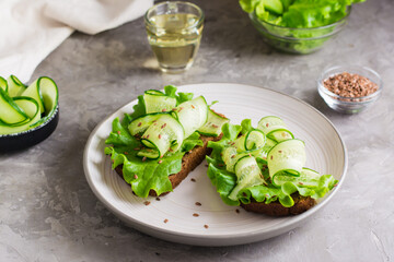 Ready-to-eat sandwiches with lettuce, cucumber and flax seeds on rye bread on a plate on the table. Healthy diet food.