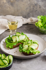 Appetizing bruschetta from rye bread, lettuce, cucumber and flax seeds on a plate on the table. Healthy diet food. Vertical view