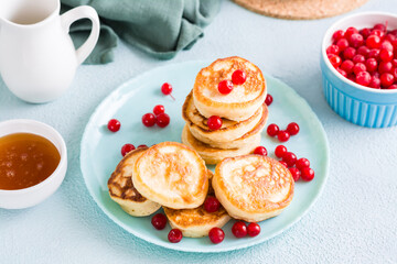 Ready to eat pancakes and cranberries on a plate and a bowl of honey on the table. Homemade breakfast dessert.