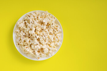 Popcorn on a yellow background. Delicious fresh homemade popcorn on a white plate. Close-up, selective focus. Top view. 