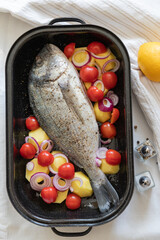 Dorade Fish with potatoes and vegetables prepared in a casserole dish for grilling