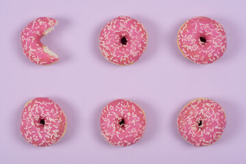 Fototapeta na wymiar Six pink icing donuts lie side by side on a pink background and are photographed from above. A pastry has been eaten