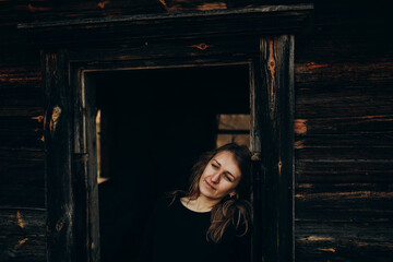 beautiful Ukrainian girl in black clothes near the old wooden house. The war in Ukraine. Portrait of a woman on a dark wooden background. Old abandoned wooden house. Old wooden window frame