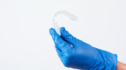 Adult man with gloves holds invisalign transparent braces for dental correction